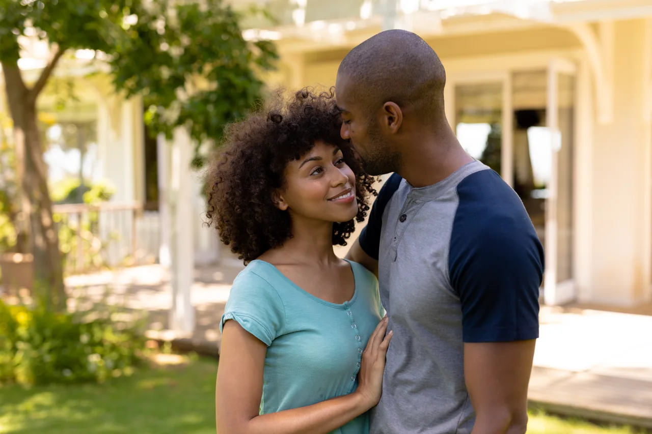 A couple sharing a forehead kiss in a sunlit garden for Black singles dating