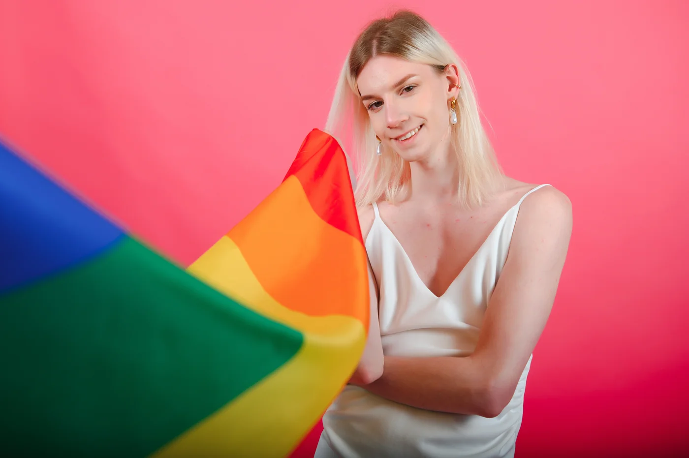 An adult woman holding a Pride flag against a red background for trans singles dating with HSV
